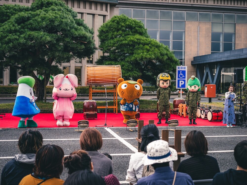 役場前の駐車場に設けられた赤いステージに、ご当地キャラクターと和太鼓が並ぶ、まちフェスの様子
